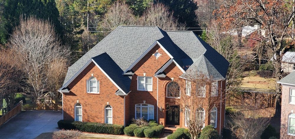 Elegant brick house with multiple gables, manicured landscaping, and driveway in sunny neighborhood.