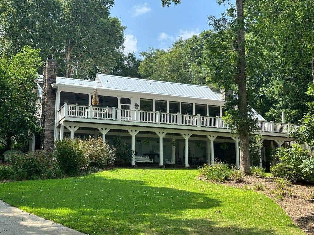 Modern white house with a metal roof, surrounded by green trees and landscaping.
